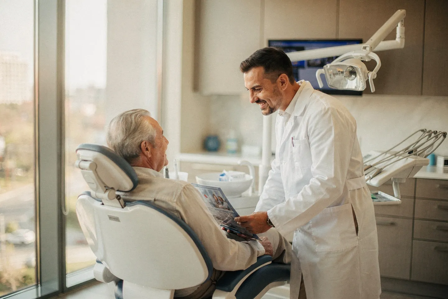 Ein freundlicher Zahnarzt berät einen älteren Patienten im Behandlungsstuhl einer modernen Praxis