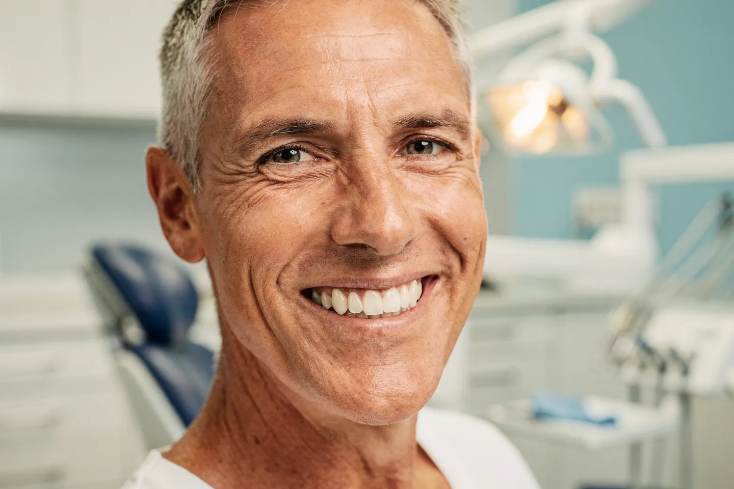 Ein lächelnder Patient mittleren Alters mit perfekt ausgerichteten weißen Zähnen in einer Zahnarztpraxis