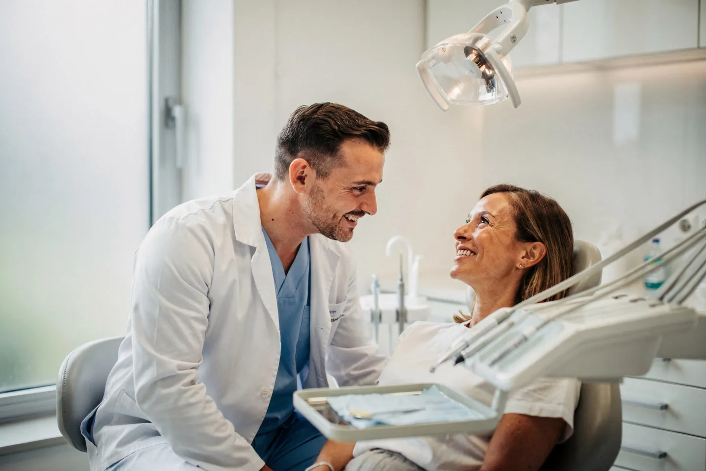 Ein freundlicher Zahnarzt berät einen lächelnden Patienten im modernen Behandlungszimmer