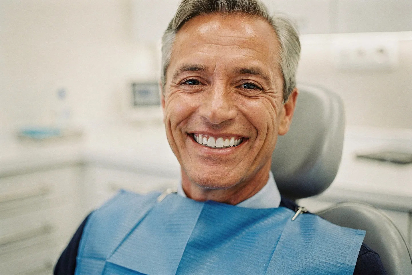 Ein mittelalter Patient mit perfekten weißen Zähnen lächelt in einer modernen Zahnarztpraxis