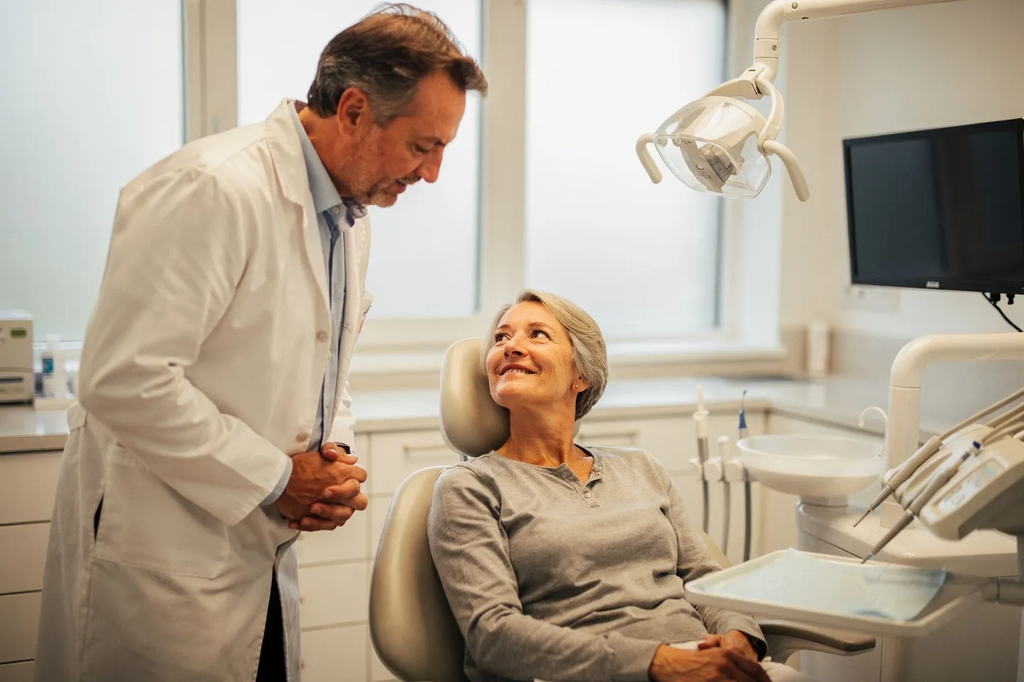 Ein freundlicher Zahnarzt hört einer älteren Patientin im Behandlungsstuhl zu