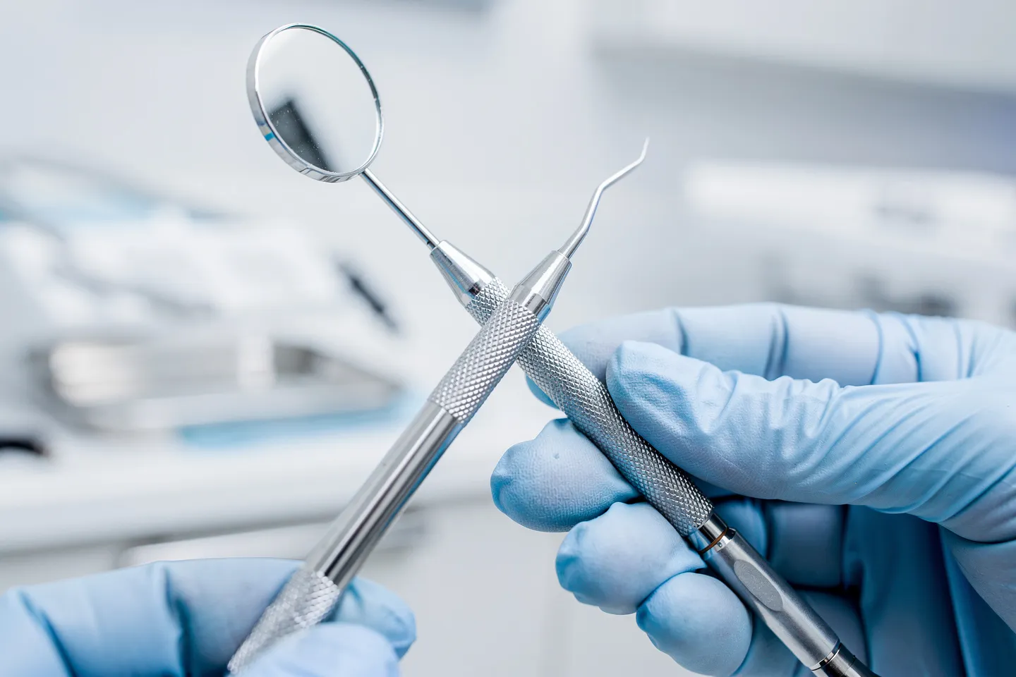 Eine behandschuhte Hand hält zahnärztliche Instrumente vor sterilen Geräten