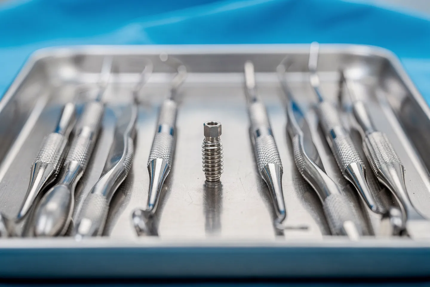 Präzise Zahninstrumente liegen ordentlich auf einem sterilen Edelstahltablett mit einem Implantat in der Mitte.