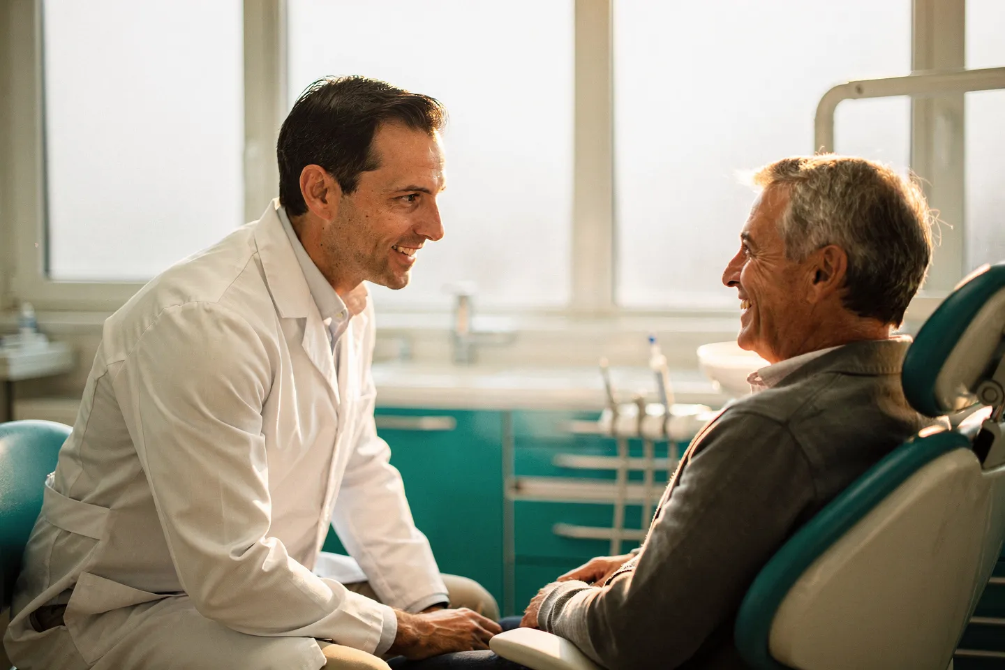 Ein freundlicher Zahnarzt in weißem Kittel berät einen lächelnden Patienten in einer modernen Praxis