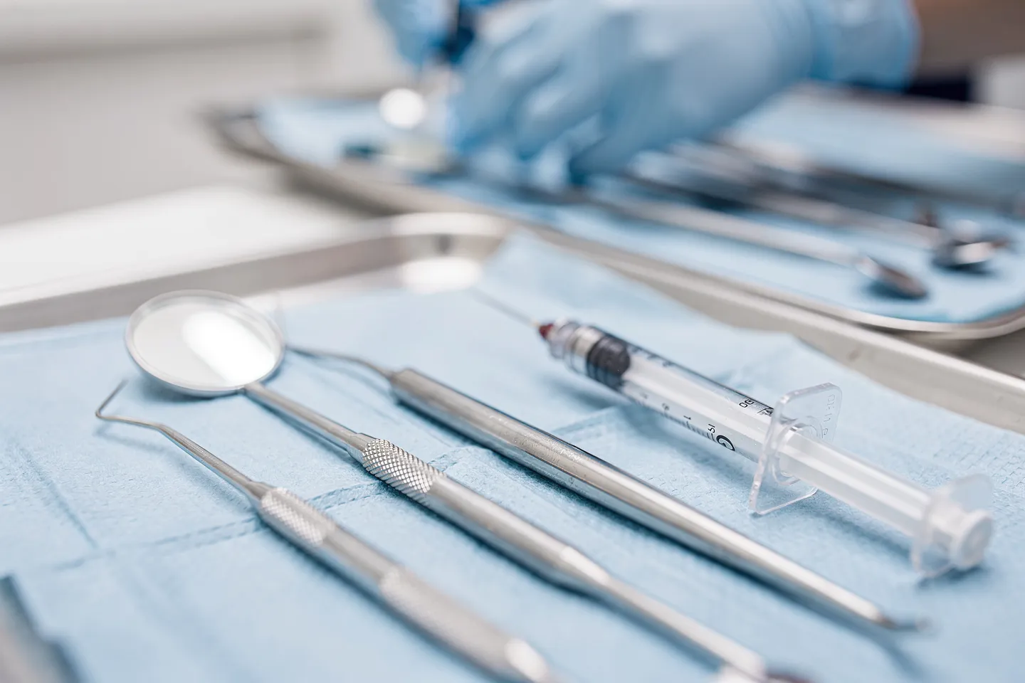 Präzise angeordnete Zahnarztwerkzeuge auf blauem Tablett mit Handschuhen im Hintergrund