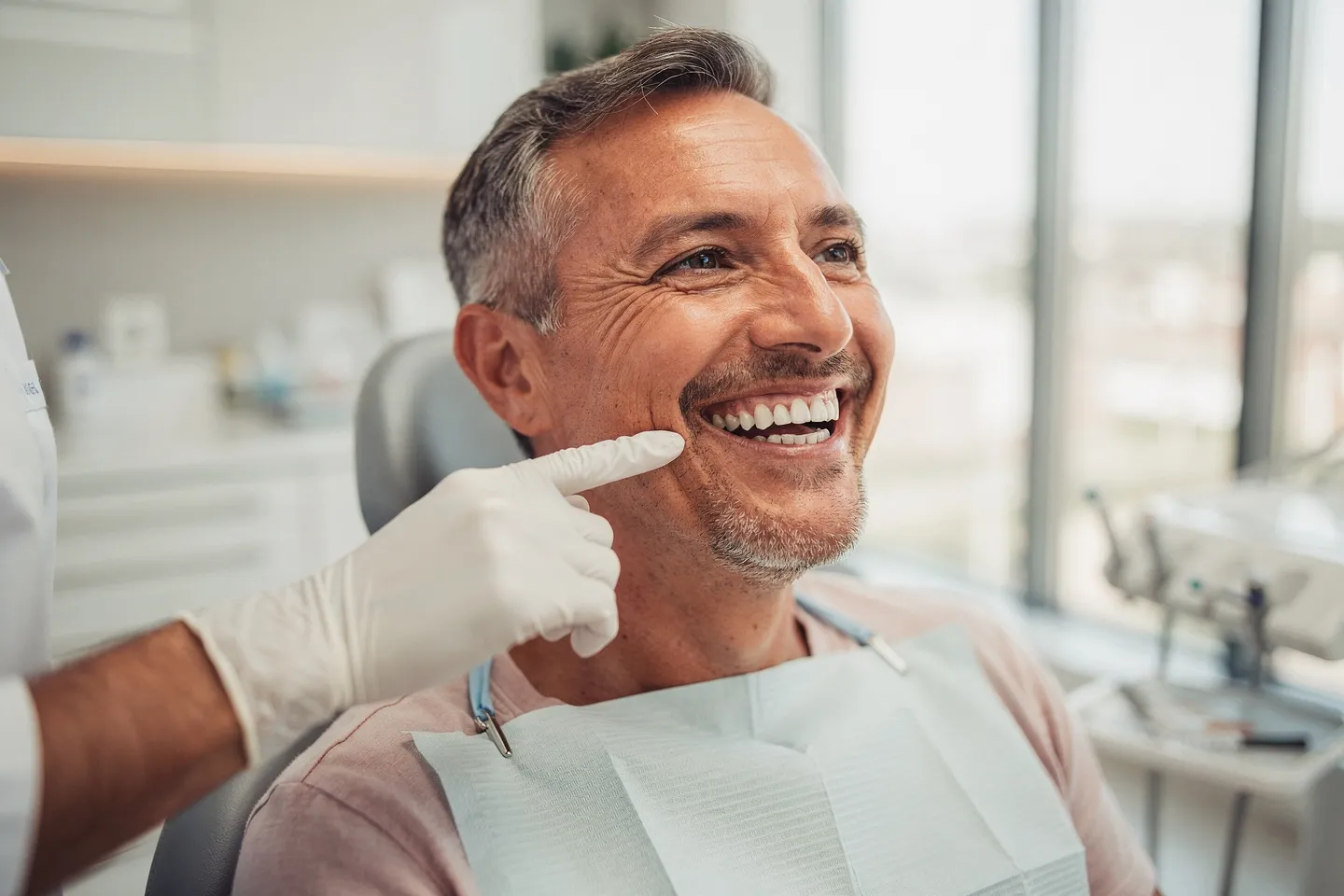 Ein mittelalter Patient mit perfekten weißen Zähnen lacht fröhlich in einer modernen Zahnarztpraxis