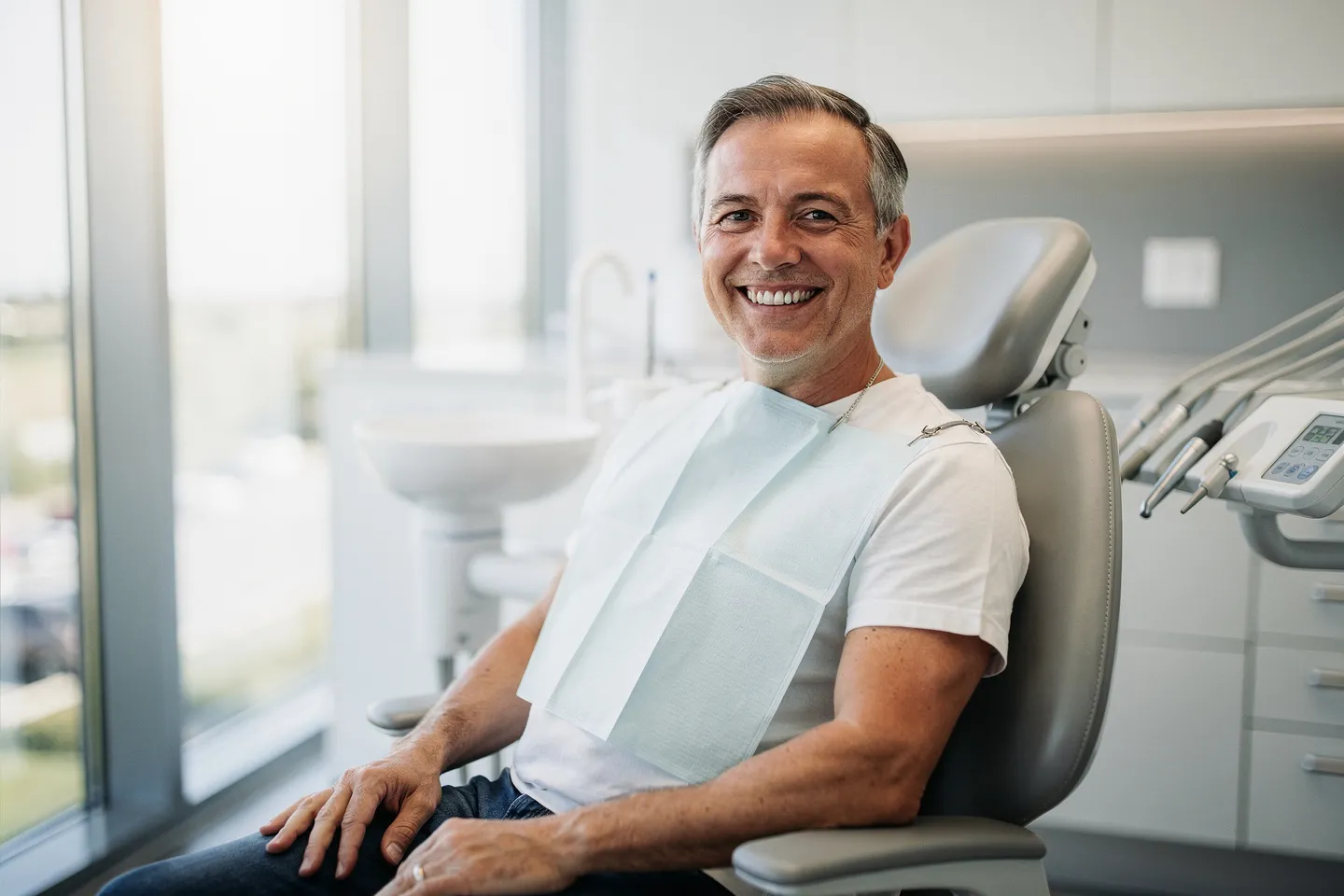 Ein lächelnder Patient mittleren Alters sitzt selbstbewusst auf einem modernen Zahnarztstuhl