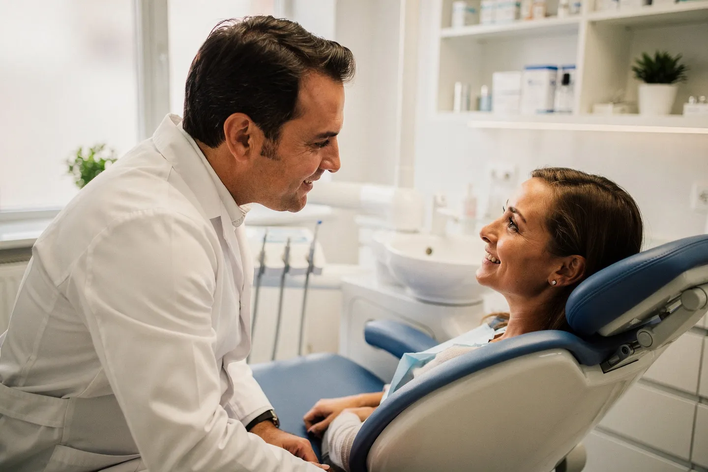 Ein freundlicher Zahnarzt in weißem Kittel berät einen lächelnden Patienten im modernen Behandlungszimmer