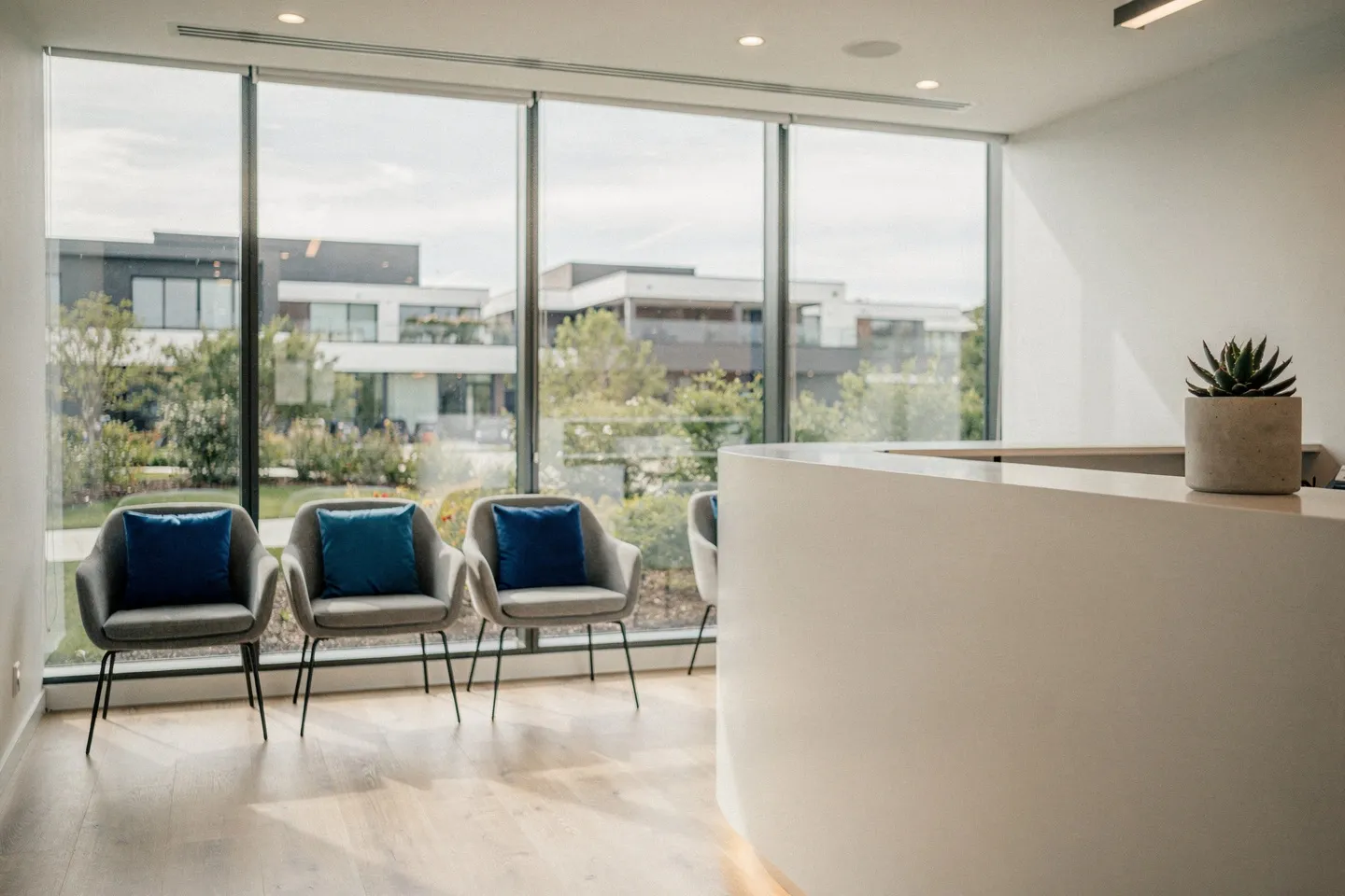 Moderner Zahnarzt-Empfangsbereich mit weißem Schreibtisch, grauen Wartesesseln und großflächigen Fenstern