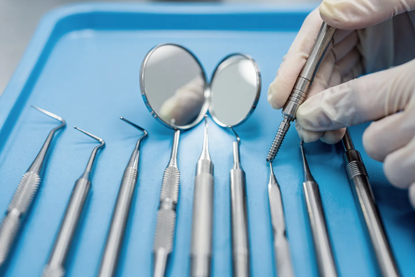 Präzise Zahnarztinstrumente liegen auf einem blauen sterilen Tablett, eine Hand mit Handschuh richtet einen Bohrer