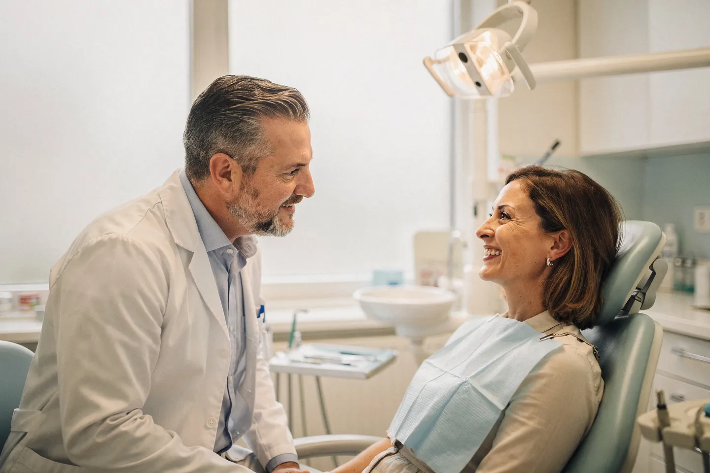 Ein freundlicher Zahnarzt berät einen lächelnden Patienten in einer modernen Praxis mit großen Fenstern