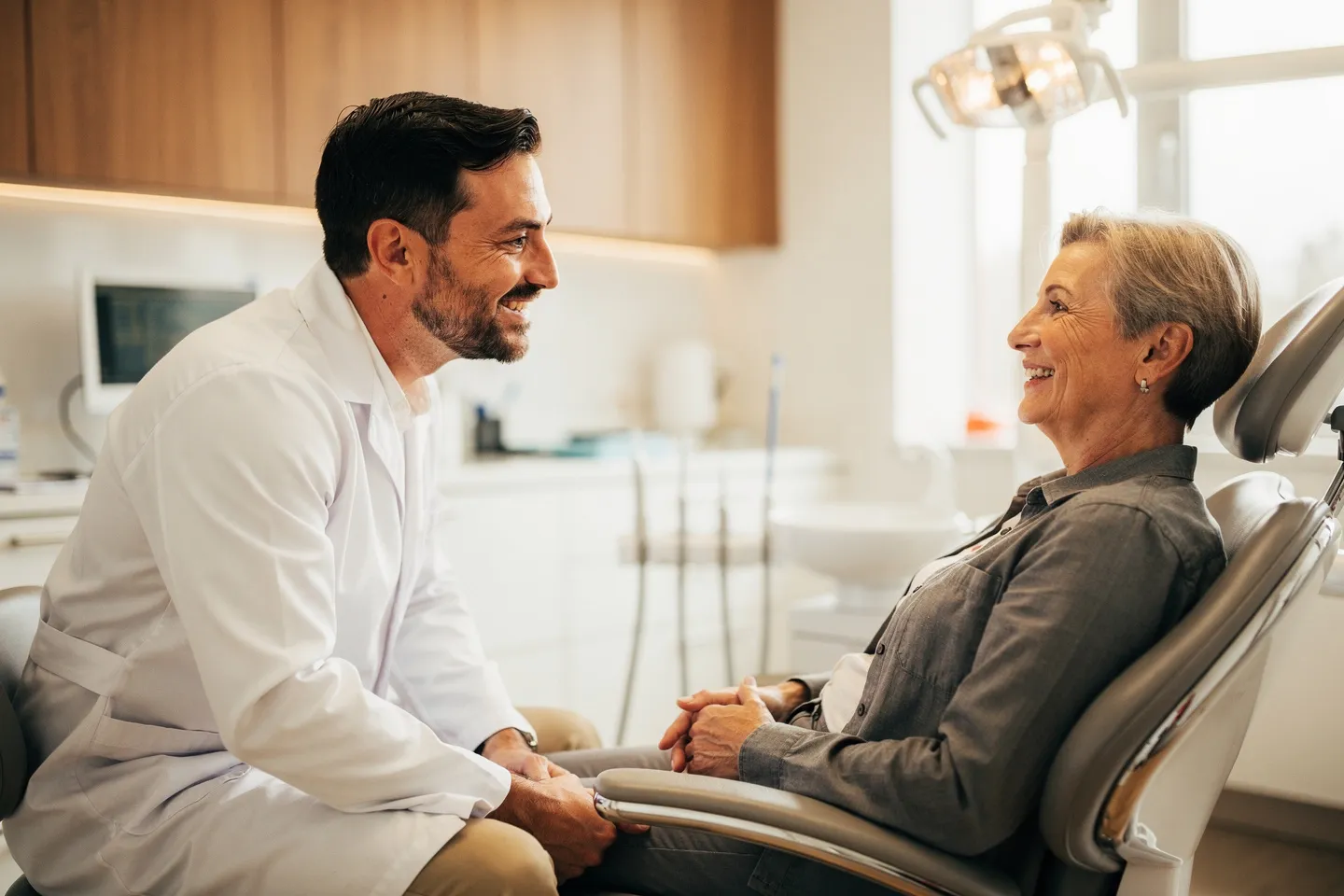 Ein freundlicher Zahnarzt im weißen Kittel spricht mit einem lächelnden Patienten in einer modernen Praxis