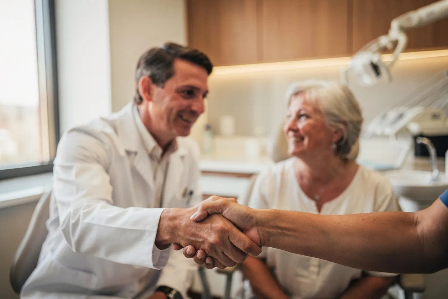 Ein freundlicher Zahnarzt in weißem Kittel berät einen lächelnden Patienten in einer modernen Praxis
