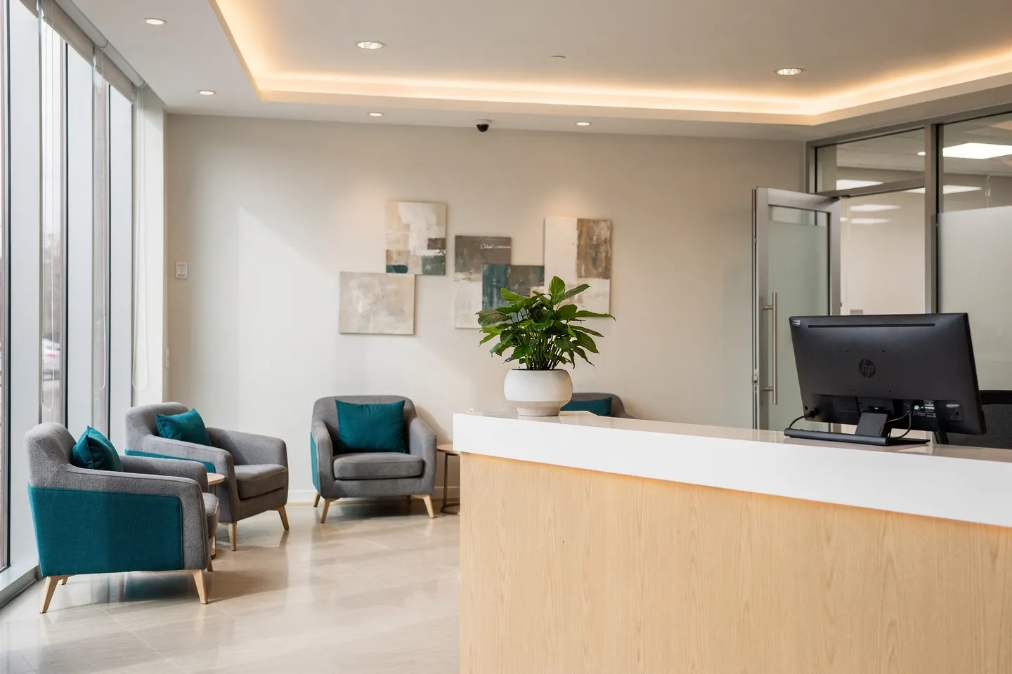 Modernes Zahnarzt-Wartezimmer mit Holzoptik, grauen Möbeln und blaugrünen Sesseln vor großen Fenstern