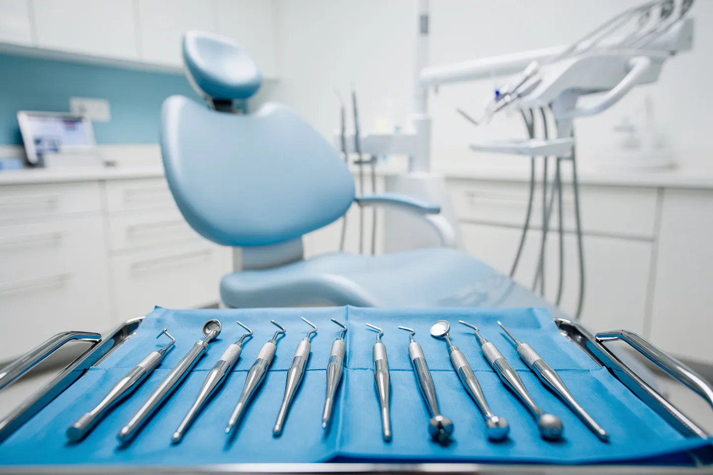 Moderne Zahnarztinstrumente auf blauem Tablett mit ergonomischem Behandlungsstuhl im Hintergrund